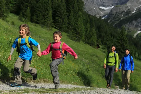 Family hiking in the mountains with children running on a forest trail